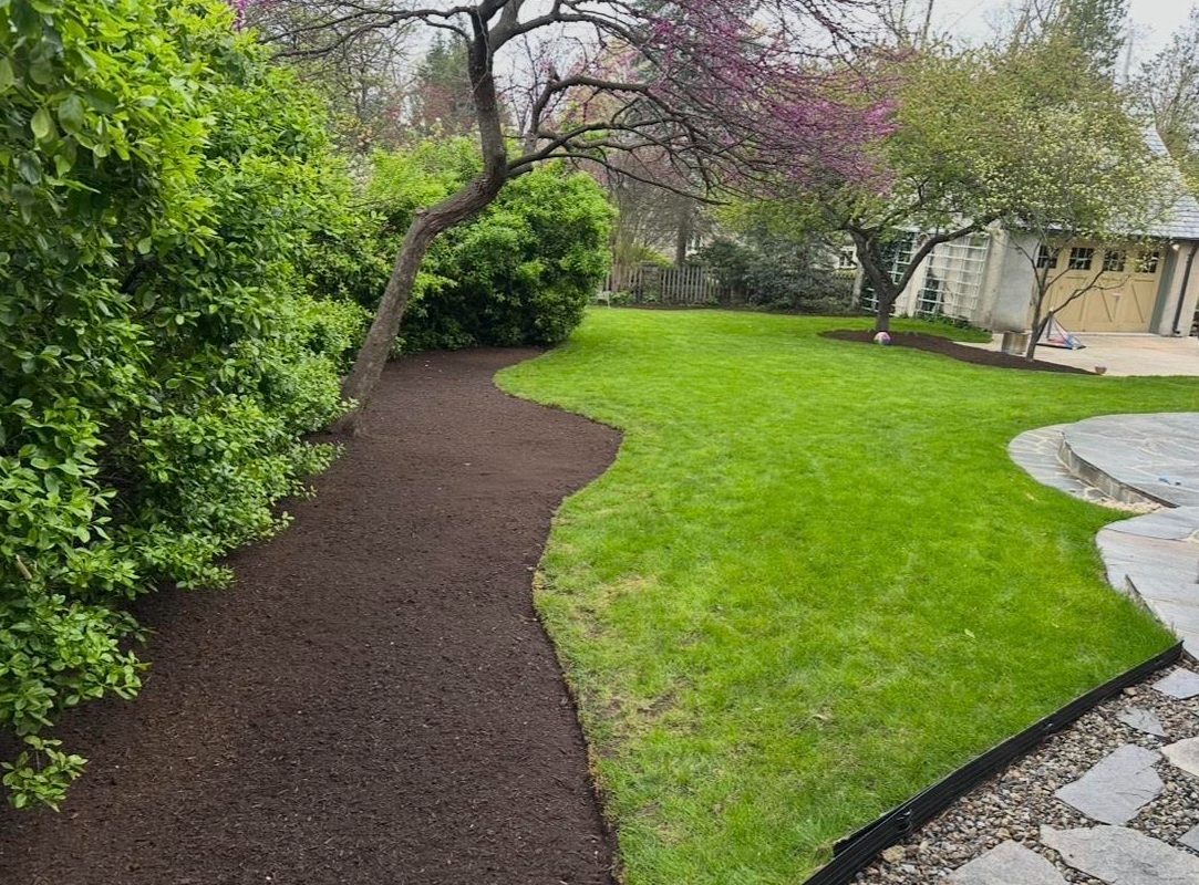 A curving bed of fresh dark mulch between shrubs and an edged lawn, with a stone patio at right